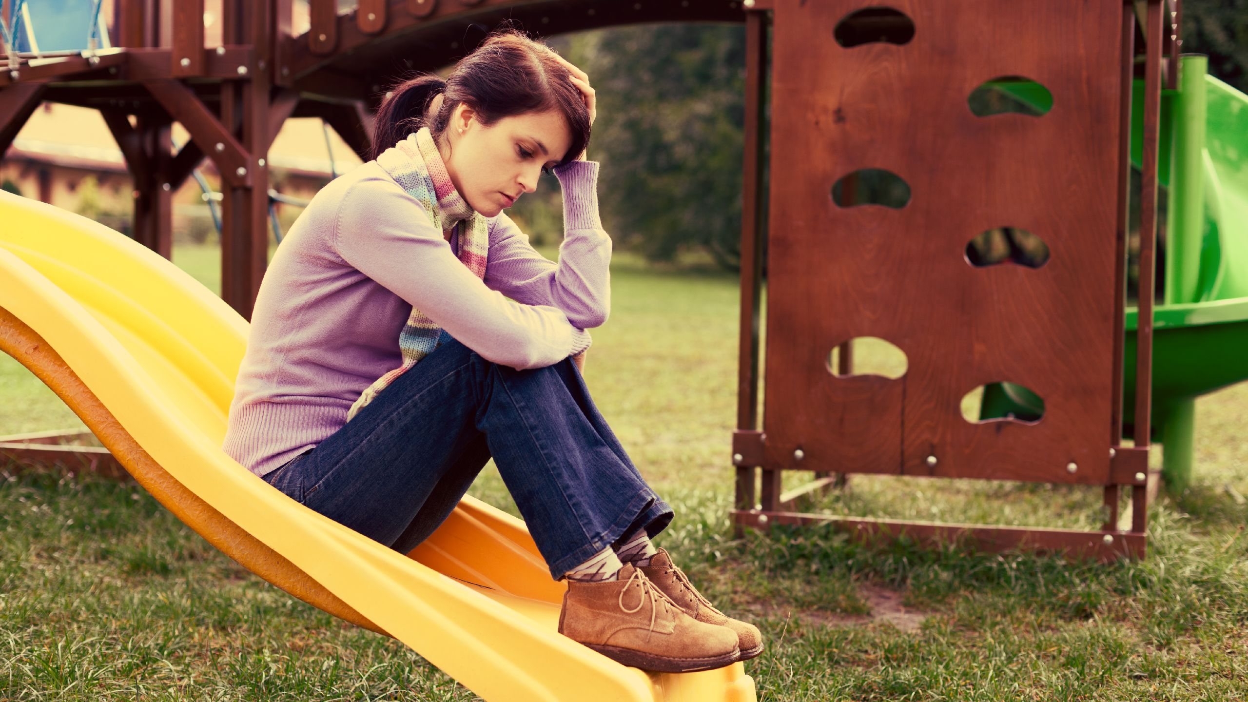 Sad young woman sitting on a children's slide with head in hands. 