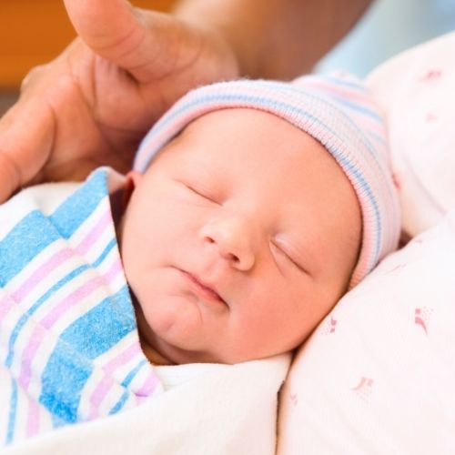 newborn baby in beanie and blanket with adult hand hovering over head