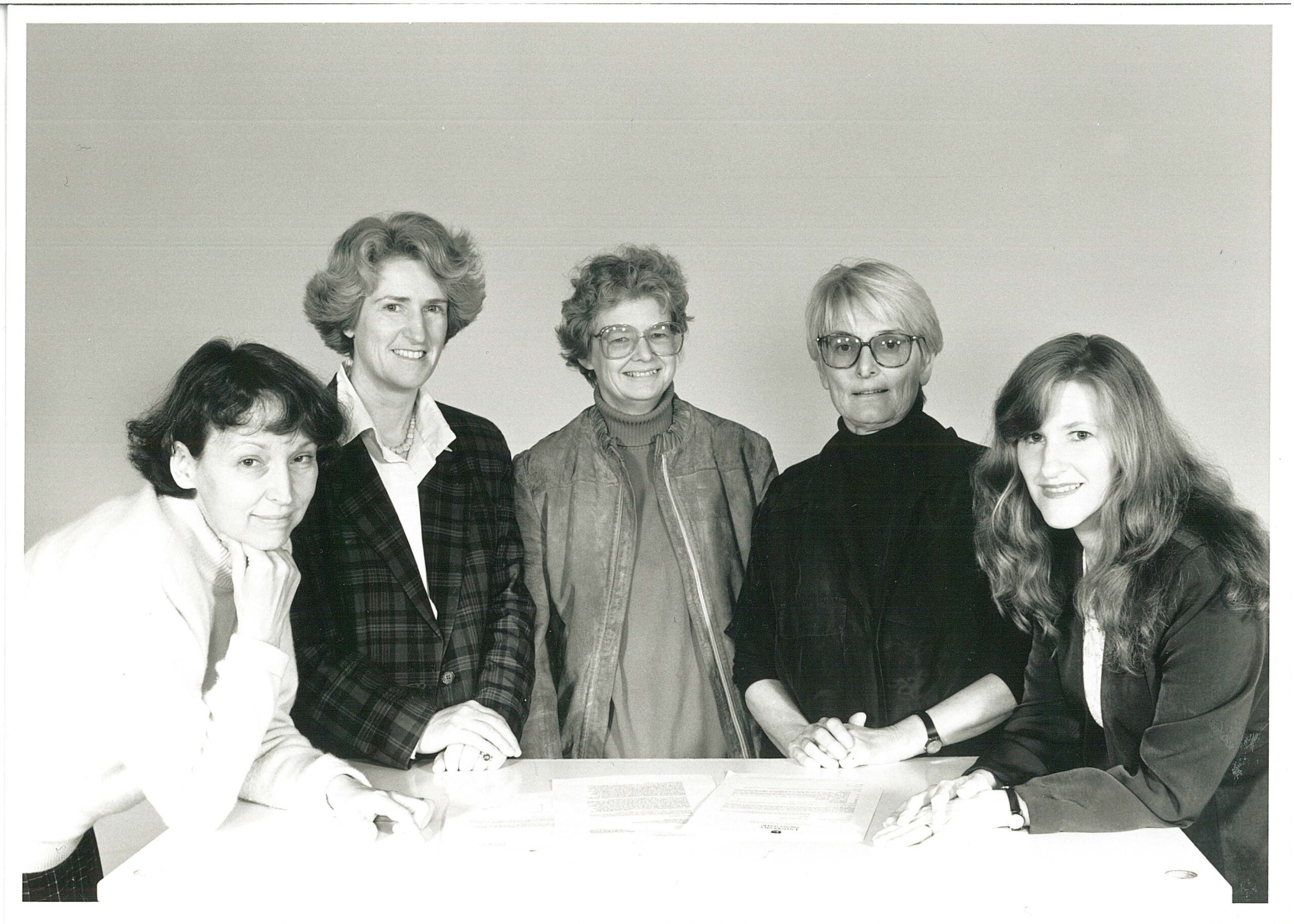 Black and white photograph of Wendy Brown, Margot Schofield, Annette Dobson, Lois Bryson, Julie Byles gathered around a table.